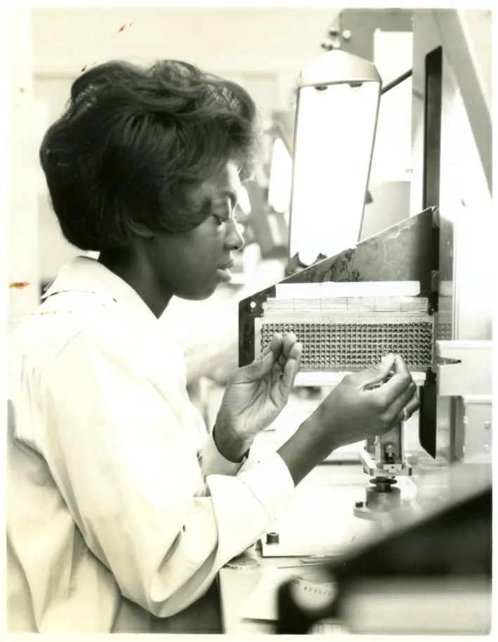 A woman at Raytheon's Waltham plant threading wire through a core rope memory module for the Apollo Guidance Computer